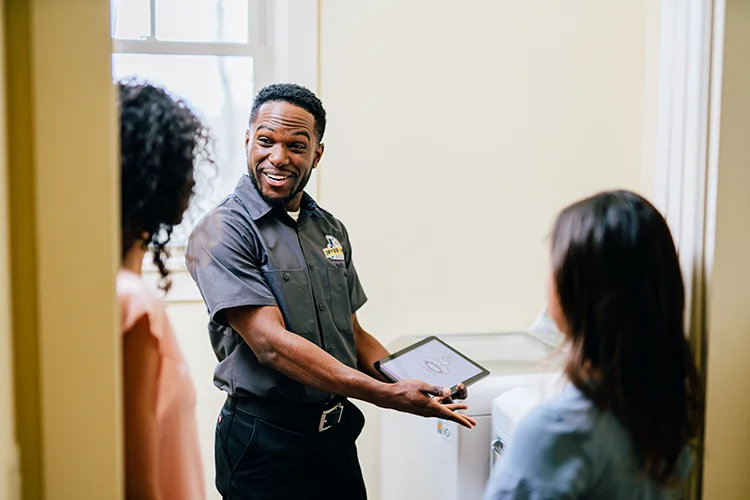 Dryer Vent Wizard tech discussing dryer vent cleaning with a family in a laundry room.