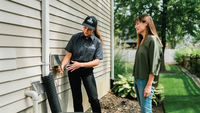 A professional from Dryer Vent Wizard holds up a dirty dryer vent line and speaks with homeowner.
