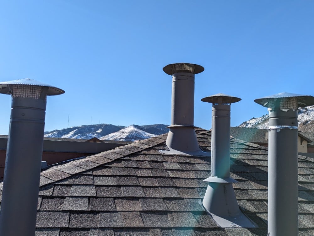 Image of three roof vents obstructed by debris, likely due to a screen covering, at an assisted living facility in Golden, CO, with the Rocky Mountains in the background