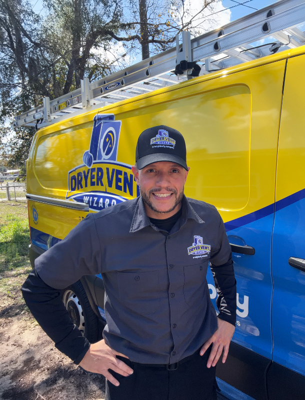 Man in Dryer Vent Wizard uniform standing in front of a branded yellow service van with a ladder on top, smiling and posing outdoors, representing a professional dryer vent cleaning and maintenance service in Tampa.