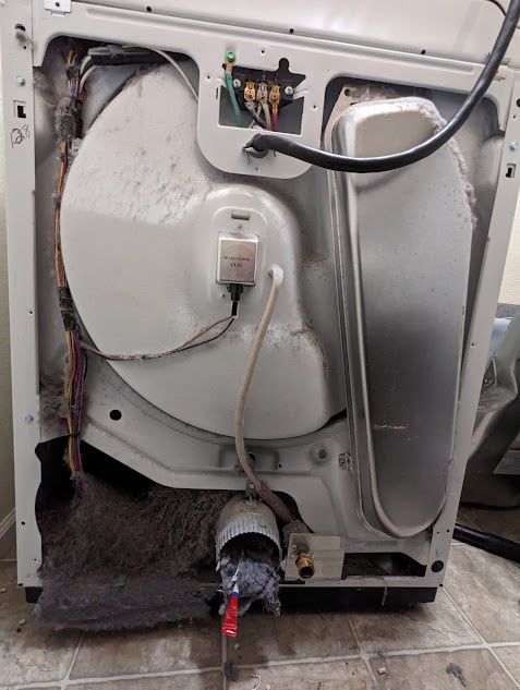 Back of a dryer opened shows extensive lint and debris accumulation, including burnt dog hair and candy wrappers, serviced in Boulder, CO