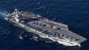An aerial view of a gray US aircraft carrier sailing on deep blue water.